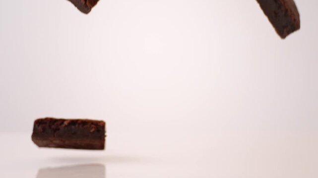 Rich fudgy brownies dropping and bouncing across white seamless backdrop in high speed slow motion. chocolate brand commercials, indulgent dessert reels, comfort food posts.