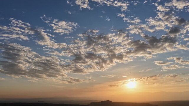 Sweeping Drone 4K timelapse of a beautiful dawn sunrise. Fast moving clouds illuminate with glowing morning light as they evolve dynamically over a vast, majestic southwest desert horizon.