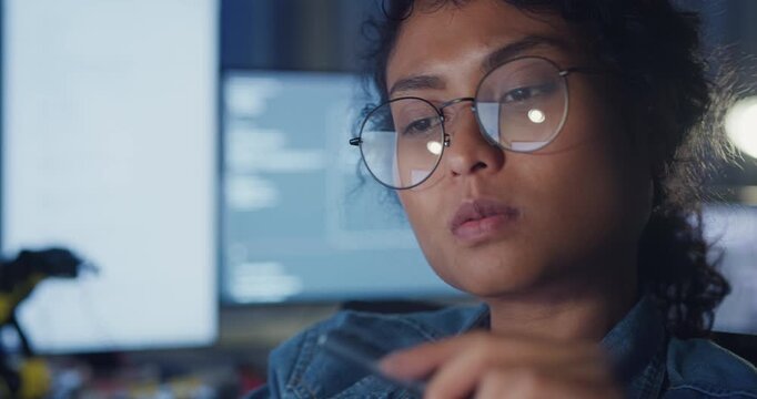 Close-up young Black female programmer coding AI software on multiple screens in night office. Network security, cybersecurity, machine learning, working late, overtime, robotics automation concept.