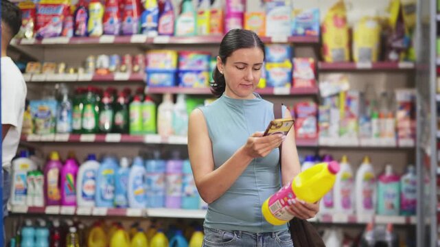 Before making purchase, young woman buyer scans barcode code on packaging of fabric liquid detergent follows link and reads information about product on manufacturers website. High quality 4k footage