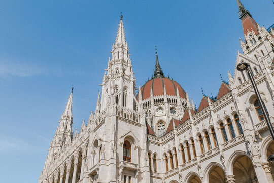 Low-angle architectural view of an elaborate historic building featuring a large red dome, soaring Gothic spire, arched windows and intricate stone ornamentation.