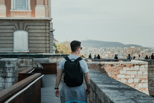 Male traveler with backpack walking along historic castle walls while exploring a European city
