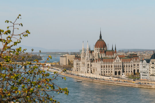 Gothic revival palace framed by green spring foliage along a scenic European river