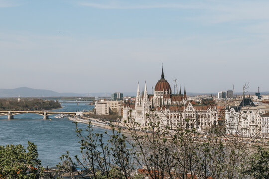 Gothic revival palace framed by green spring foliage along a scenic European river