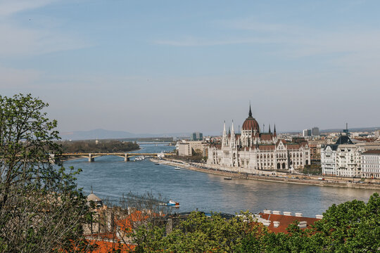 Gothic revival palace framed by green spring foliage along a scenic European river