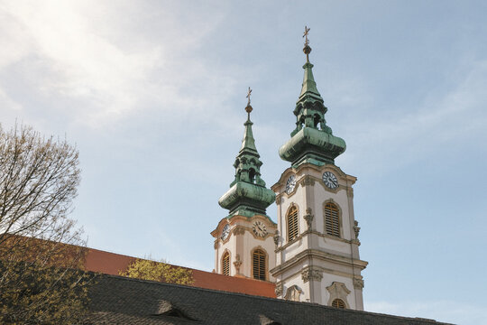 Twin Baroque church towers with green copper spires and clock faces against blue sky