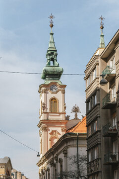 Historic Baroque church tower with green copper spire rising above urban buildings