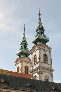 Twin Baroque church towers with green copper spires and clock faces against blue sky