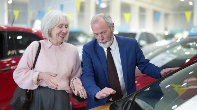 Elderly woman carefully examines the car before buying. Pensioner stands in a car dealership and looks at the assortment of cars. High quality 4k footage
