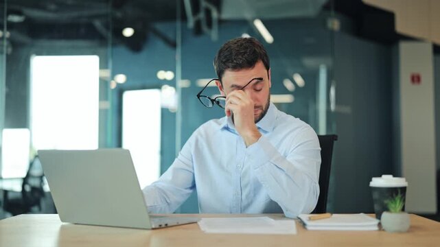 Close-up of tired businessman or IT specialist feeling eye strain and headache at computer. Overworked corporate worker, manager or freelance designer suffering from fatigue or migraine at office desk