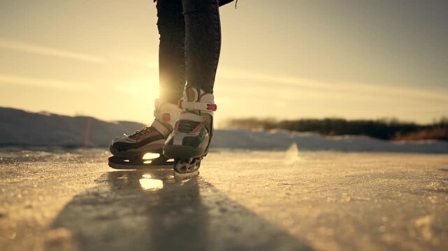 Person glides wearing ice skate. Beautiful winter sunset shines upon frozen lake. Sharp blade cuts cold ice. Outdoor skating brings true joy during winter. Sun creates warm glare near skate.