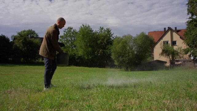 Wide outdoor shot of a man spreading fertilizer over a residential lawn, useful for garden care, landscaping, home maintenance, sustainability and healthy grass growth themes