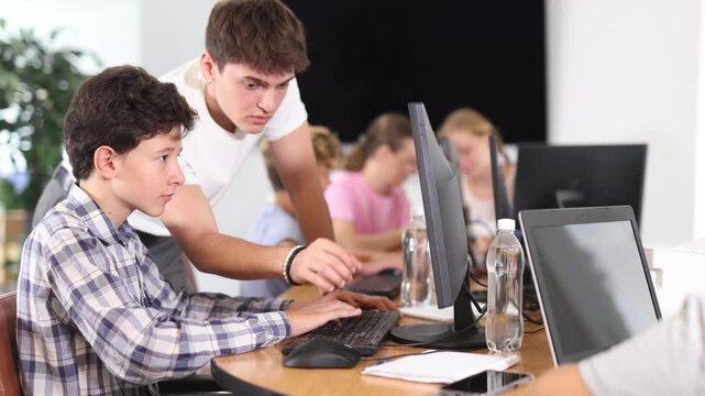 Concerned boy sitting at computer while trainer explaining him something during IT courses
