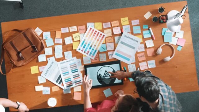 Top view of smart designer holding color palette while project manager looking at design and choosing color for program. Professional businesswoman taking a note while design creative logo. Symposium.
