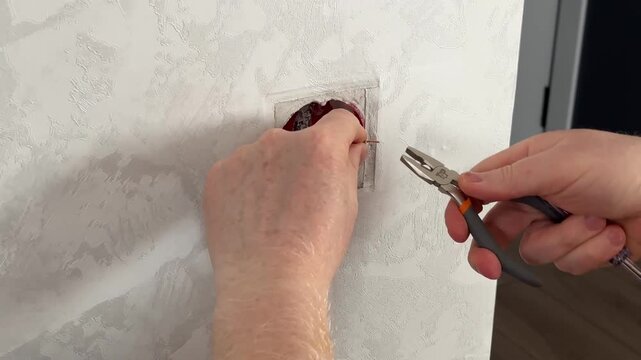 The electrician installs the outlet using pliers. Cutting the wires in the outlet. Light switch mechanism