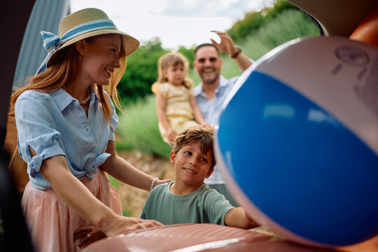 Happy little boy packing a beach ball into car trunk while getting ready for summer holiday with his family.