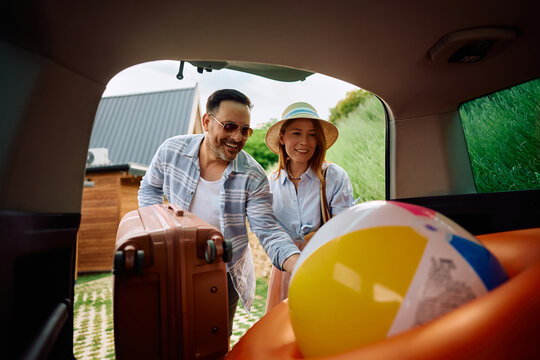Happy couple packing their belongings into car trunk while going on summer holiday.