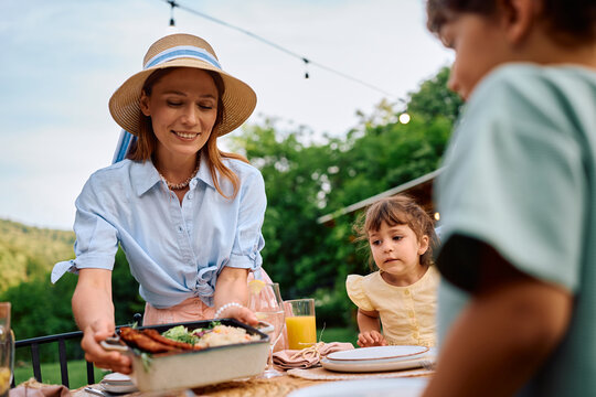 Happy mother serving food during family meal on terrace.