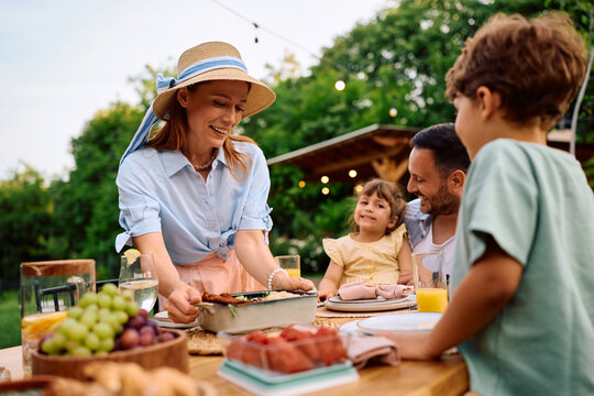Happy woman bringing food at table during family meal on terrace.