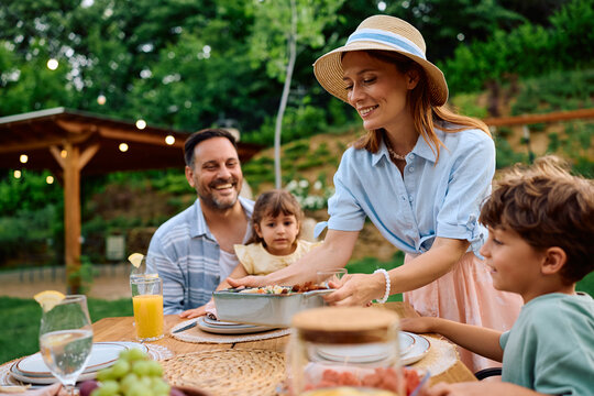 Happy mother serving food while having lunch with her family on patio.