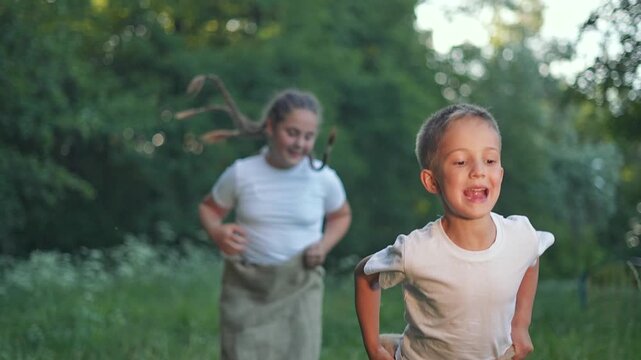 Boy runs ahead in competition. Girl child follows close behind jumping outdoors. Kid plays energetic game. Summer sack challenge for children. Girl and boy show jumping speed in game outdoors.