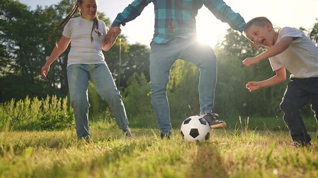 The boy and girl, full of energy, are playing a soccer game with their father. The football is central to their fun. The man encourages the children as they continue playing happily together.
