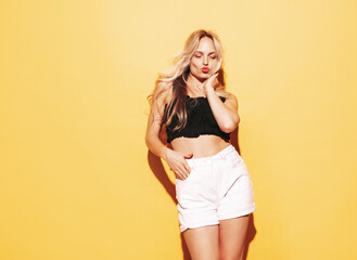 Fototapeta premium Young beautiful smiling blond female in trendy summer shorts clothes. Sexy carefree woman posing near yellow wall in studio. Positive model having fun. Cheerful and happy