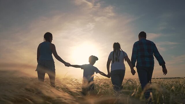 Children holding parents hands walking on path. Family walking together in summer field. Son walks near father. Daughter smiles at mother. Parents enjoy walking. Kids follow walking with family
