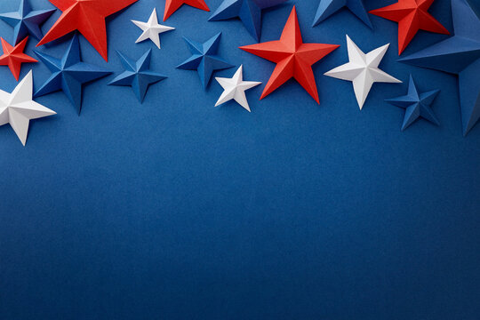 Festive arrangement of red, white and blue paper stars and curled ribbons on dark blue background. Patriotic border with empty space for text, suitable for Independence, Fourth of July, Memorial