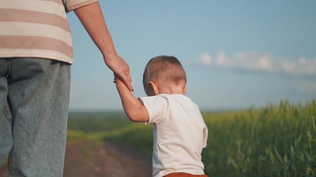 Mother walks near child along road. The boy, a curious kid, stays close to the parent on the summer path. Mother guides child, boy asks, kid points to field. Parent smiles during the summer road walk.