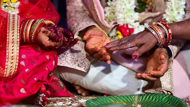 Close-up footage of bride and groom hands participating in traditional Hindu wedding rituals during a marriage ceremony in India. The scene captures sacred customs, ceremonial offerings