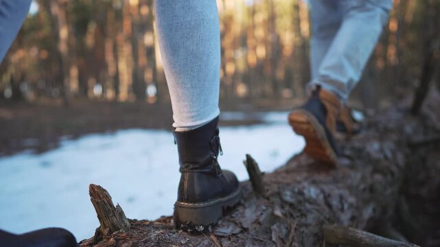 Adventurer's brown hiking boot steps carefully along weathered fallen tree trunk during wilderness trek. Rugged outdoor footwear with thick sole navigates natural log obstacle on sunny forest trail.
