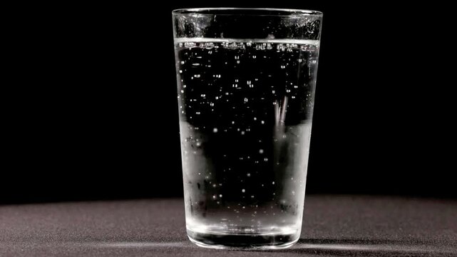 Effervescent soda water with active fizzing bubbles inside a clear glass isolated against a dark backdrop.
