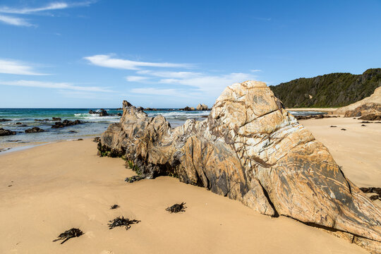 A large metamorphic rock, with strange folded and circular marks, on the beach in an ancient geological subduction zone in this stunning coastal landscape at Narooma in New South Wales, Australia.