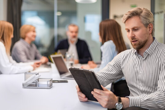 Modern business man in formalwear using digital tablet while sitting in the office, colleagues on the background