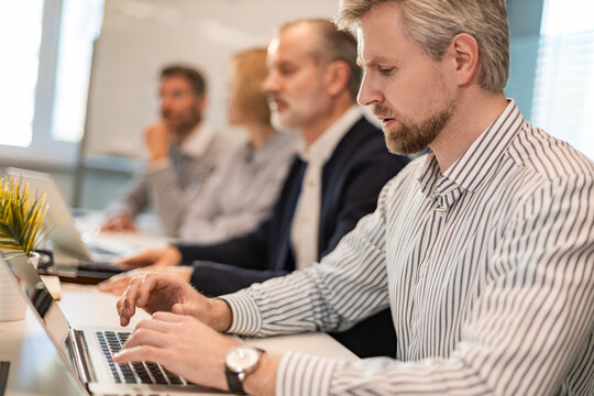 Four business professionals using laptop on desk discussing strategy company