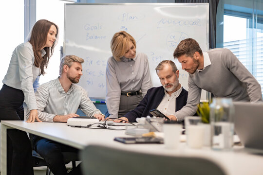 Business people discussing work together using a tablet and laptop taking notes in a modern office