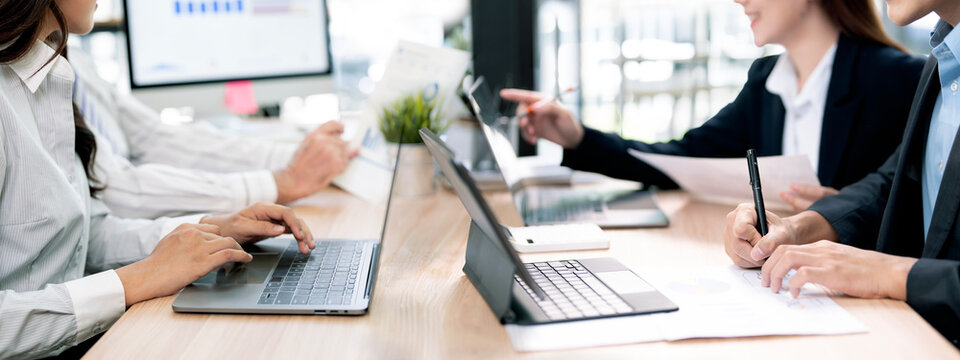 Diverse business team working together with laptops and tablets in office banner.