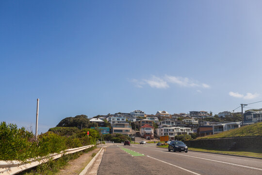 Coastal houses on hillside seen from road with car traveling through city