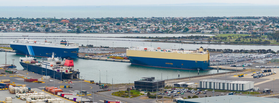 Aerial panorama view of ships at port surrounded by containers and rows of parked cars