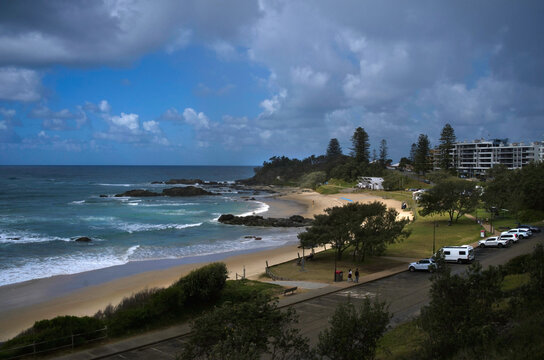 Beach with trees and buildings, sun and clouds
