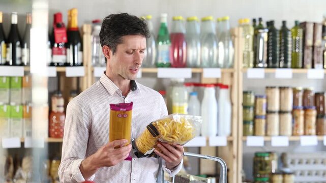 Adult man buyer chooses pasta in package in grocery store