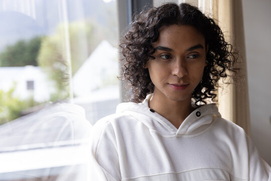 Non-binary adult standing by window, wearing offwhite hoodie and showing reflection, copy space