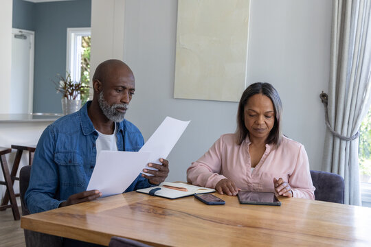 African American couple reviewing papers at dining table at home, denim shirt, pink top and tablet