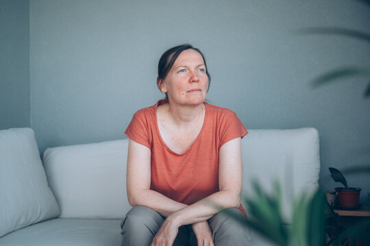 Hopeful middle-aged woman deep in thought indoors, gazing upward with a positive outlook, contemplating decisions, goals, personal growth, and life aspirations.