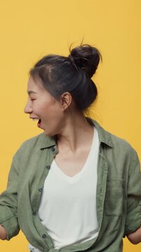 Vertical Screen : Confidence Asia youth lady stand over yellow background open palms points away on copy spac show empty space, presenting advertisement smiling excited. Mock up copy space concept.