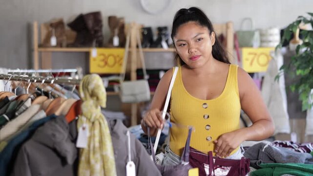 Latina chooses underwear in a clothing store, she holding bra sets in her hands and carefully examining the options on hangers. Brazilian woman buys comfortable bras in a lingerie boutique
