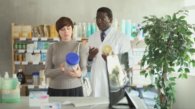 Adult woman buyer choosing baby formula with help of adult man pharmacist in pharmacy