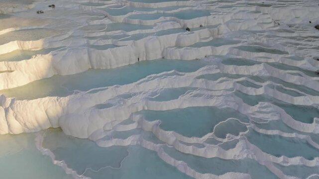 Explore the remarkable travertine terraces of Pamukkale, Turkey, known for their vibrant turquoise waters and unique mineral formations. Experience this natural wonder from above during golden hour.