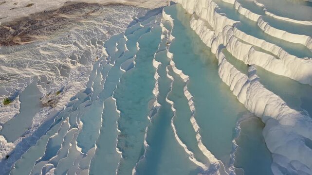 Experience the breathtaking beauty of Pammukale, Turkey as sunlight casts a golden glow on the magnificent white travertine terraces and the soothing thermal waters flow gracefully.
